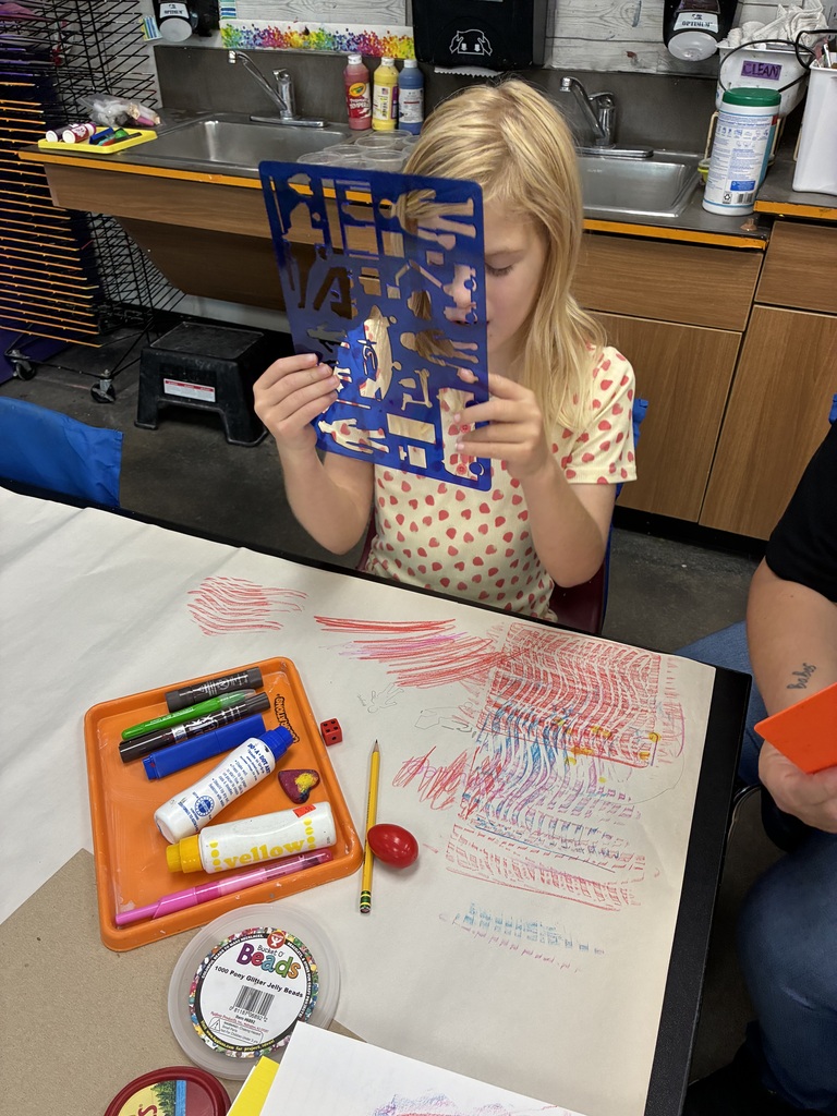 Girl looking through a stencil and a big art paper with red, blue purple colored on it 