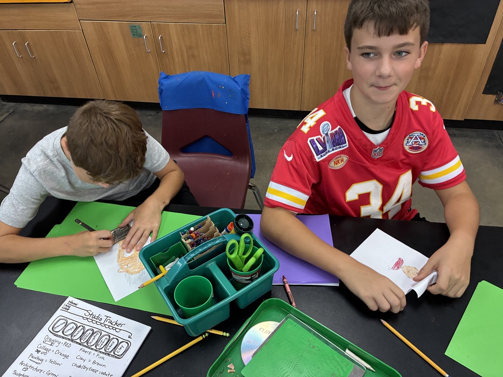 two students drawing a self portrait. One student is wearing a Kansas City Chiefs jersey