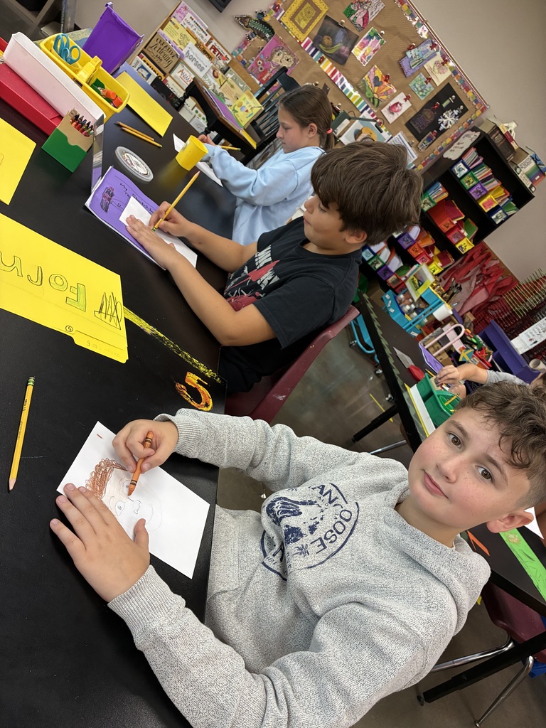 three students drawing portraits. One boy is wearing a gray sweatshirt 