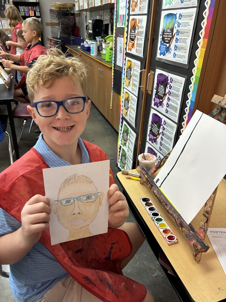Student blue shirt holding his drawing of himself