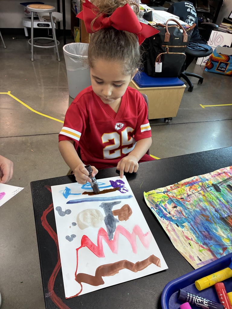 Kindergarten student with paint stick painting lines and colors.