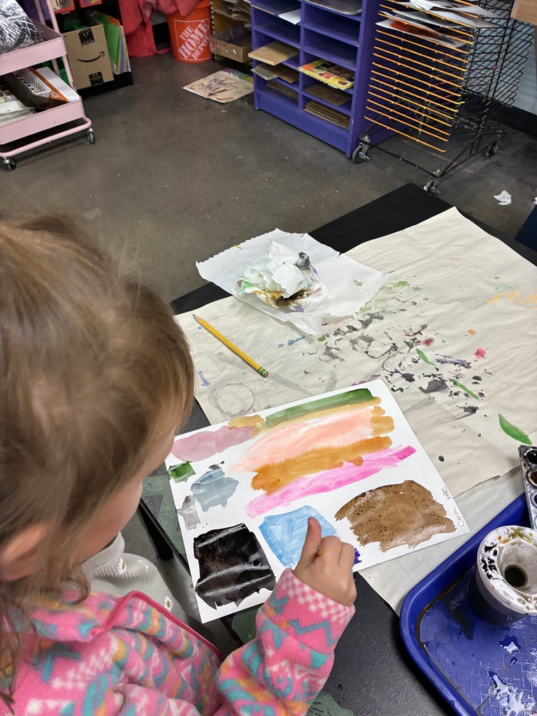 Kindergarten student with paintbrush painting lines and colors.