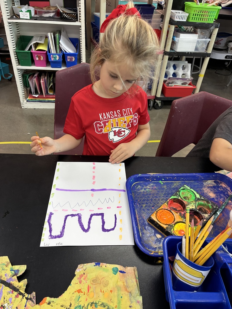 Kindergarten student with paintbrush painting purple lines and colors.