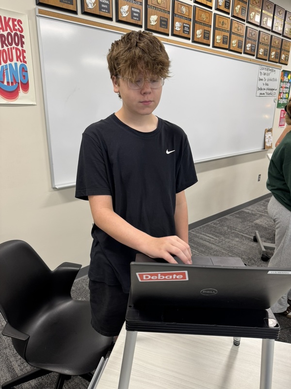 high school student standing at a portable podium with his laptop open, practicing speaker drills