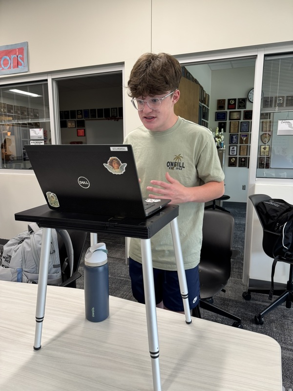 high school student standing at a portable podium with his laptop open, practicing speaker drills