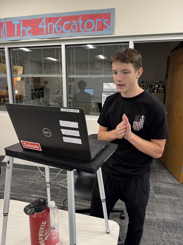 high school student standing at a portable podium with his laptop open, practicing speaker drills