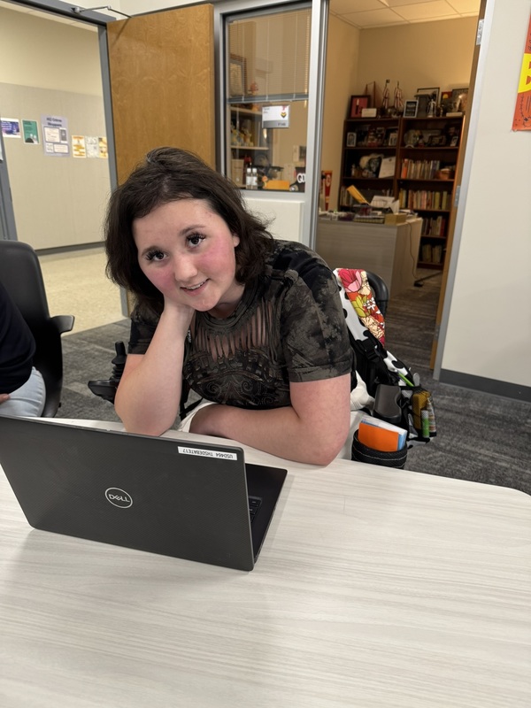 high school student wearing black shirt, sitting at a white table with her laptop open
