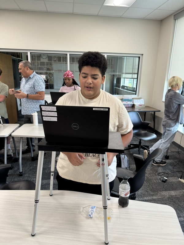 high school student standing at a portable podium with his laptop open, practicing speaker drills