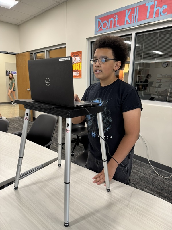 high school student standing at a portable podium with his laptop open, practicing speaker drills