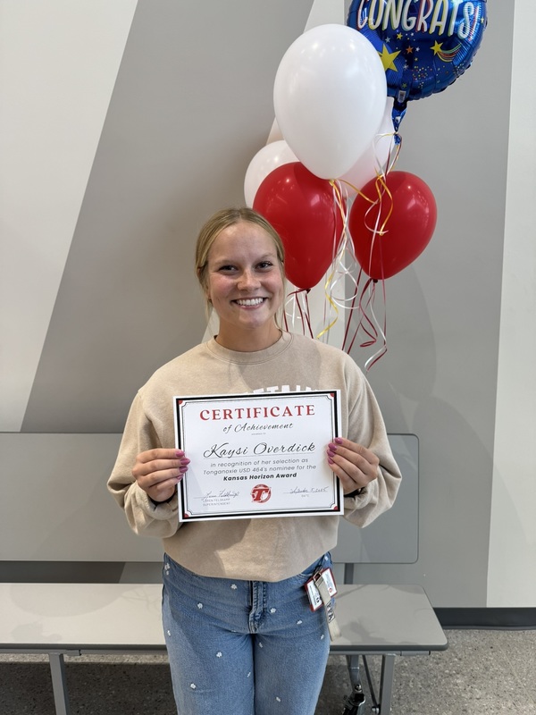 kaysi wearing beige sweatshirt and jeans, holding a paper certificate