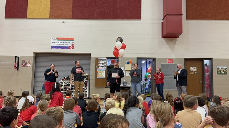 phillip brice holds balloons and certificate in TES gym as students and administrators look on