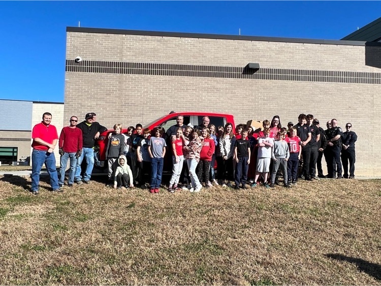 mrs. Mae’s class stands in front of trucks loaded with canned goods
