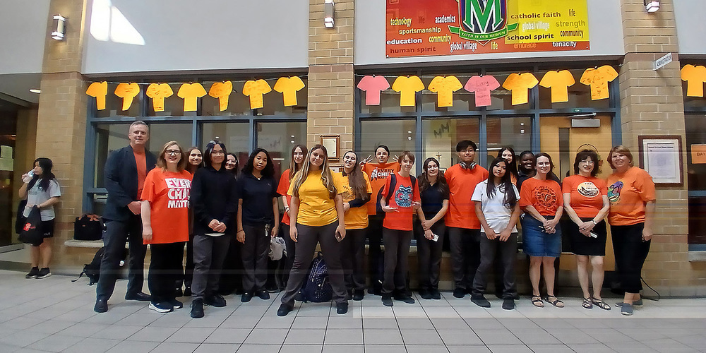 Group photo of Marshall McLuhan students and staff in front of a display of cardboard orange shirts