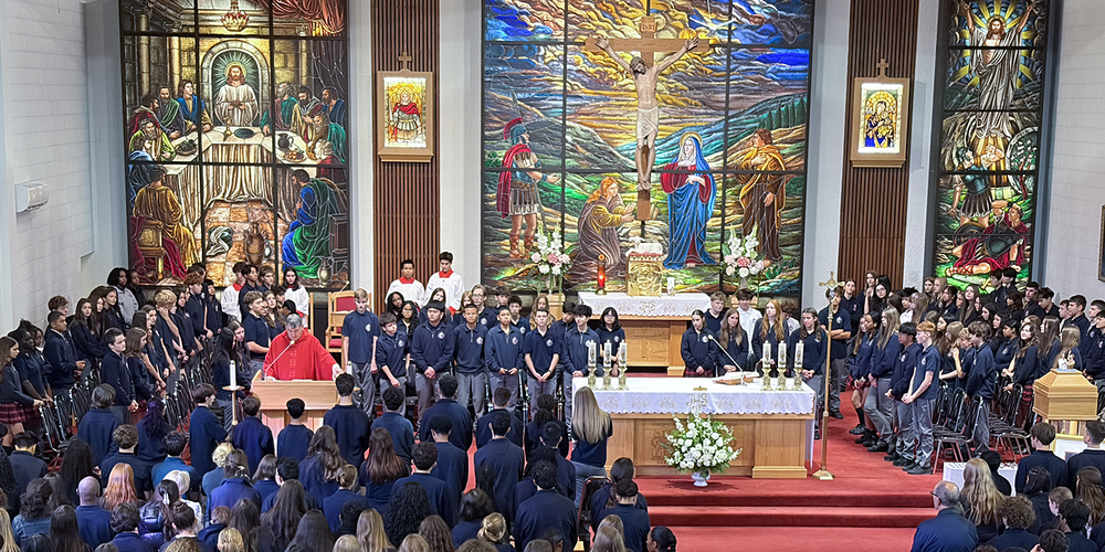 Redmond students and staff attend the Mass in the church, facing the spakers with huge sweeping religious stained glass mural artwork beyond the speakers