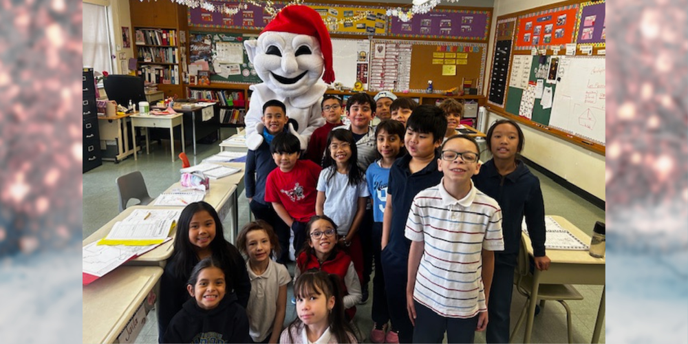 A group photo of young students in a classroom posing with Bonhomme