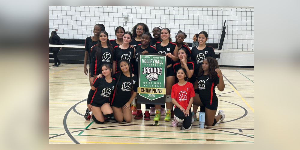 A volleyball team posing in a gym with a champions banner