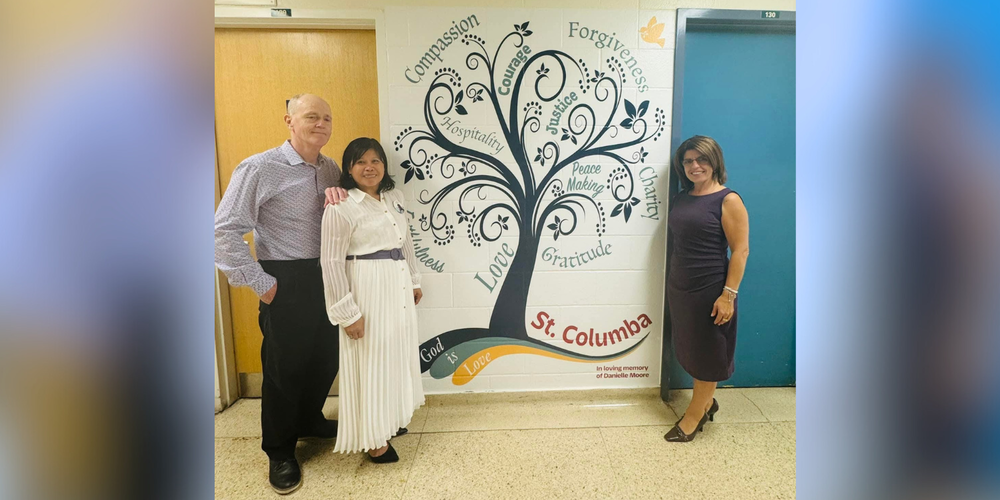 3 adults posing in front of a St. Columba mural
