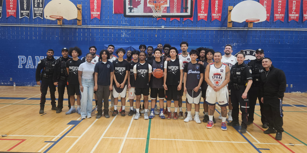 Large group photo - boys basketball team posing with police officers in a gym.