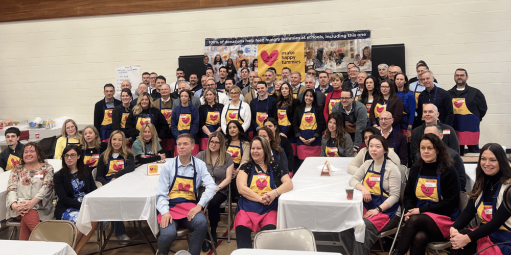 A large group of people in aprons with hearts on them, in front of "make happy tummies" banner