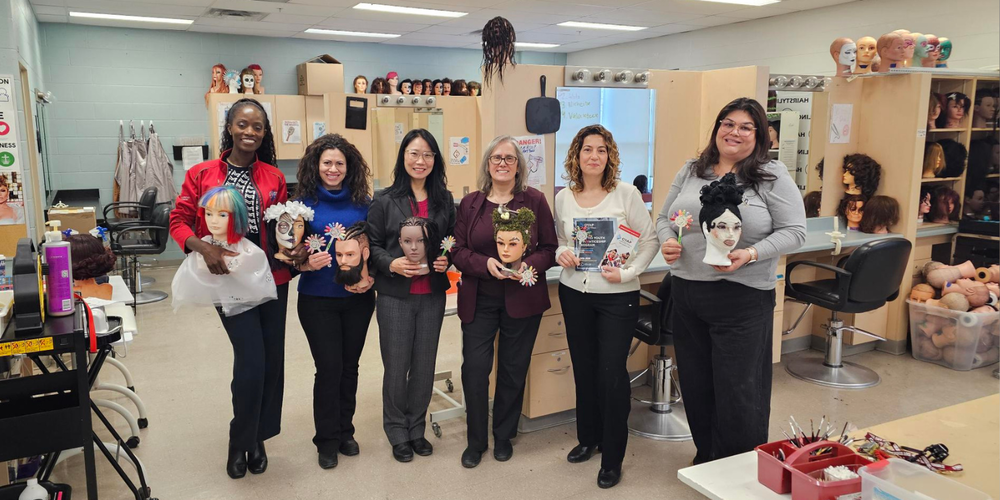 Six women posing in a beauty school type room, holding mannequin heads