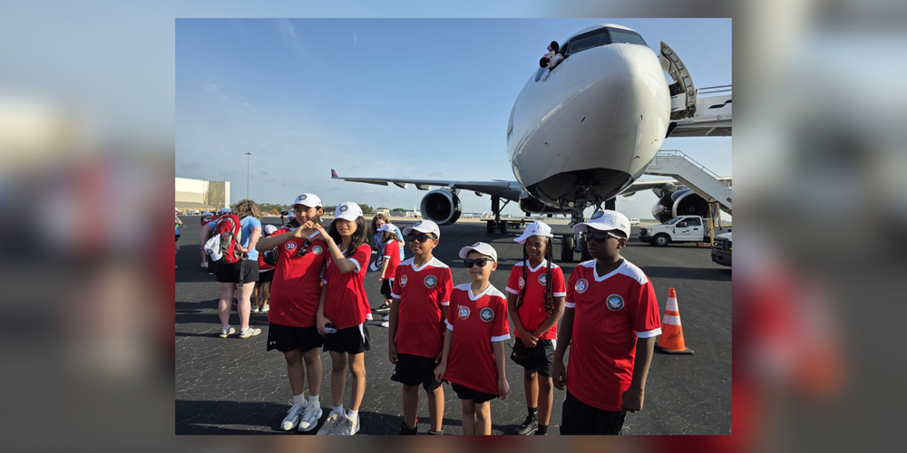 Kids wearing red, standing in front of an airplane.