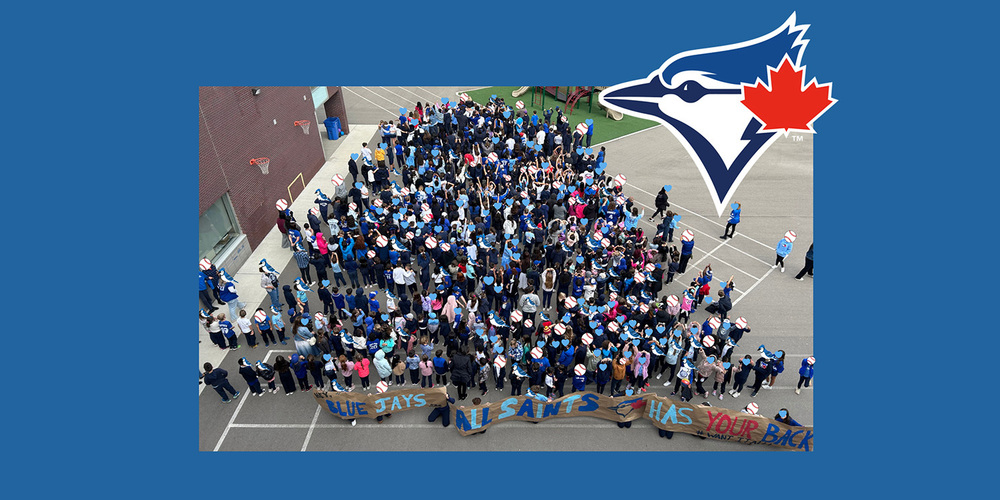 Bird's eye view group photo of the All Saints students standing together holding a banner that says "BLUE JAYS ALL SAINTS HAS YOUR BACK" for Blue Jays day