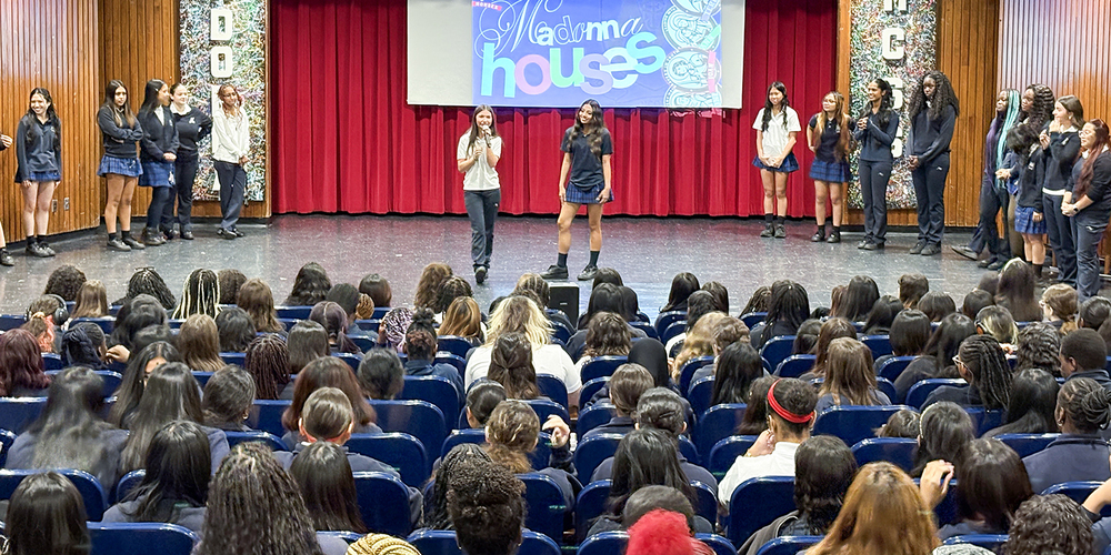 Photo of the organizing students speaking to the other Madonna students about the new House system, with a presentation on the projector screen behind them