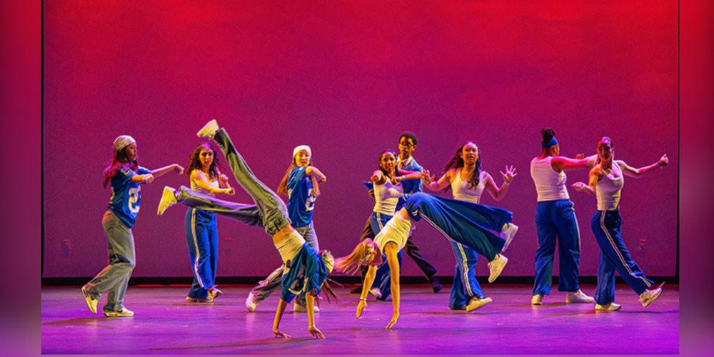Dance group on a stage lit with pink lights.