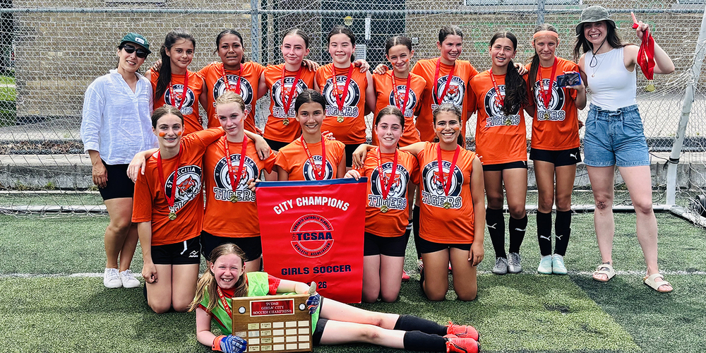 Group photo of the St. Cecilia soccer team posing on the field with their championship banner and plaque