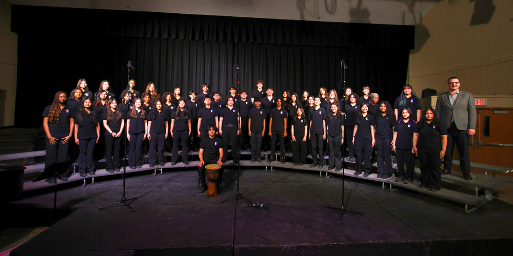 Large group[ choir standing in a dark room, all in uniforms. 