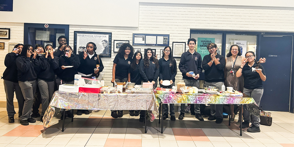 Photo of Father Henry Carr students posing together behind two tables holding food of Latin and Hispanic cultures for the students to appreciate