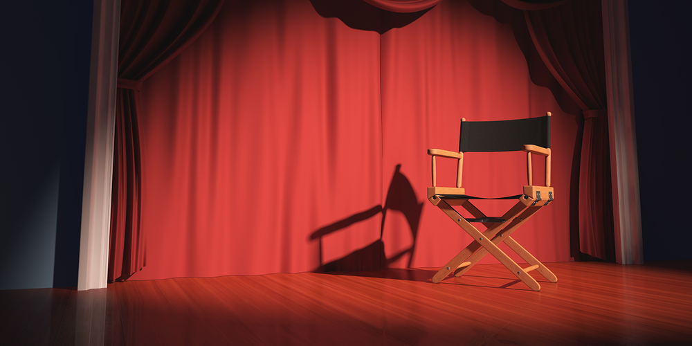 Photo of a director's chair on the stage illuminated by floodlights.