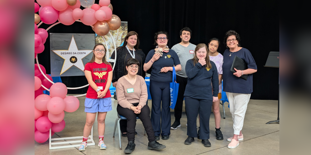 Group of students with faculty, and balloons behind with a star poster that reads "Desiree Da Costa"