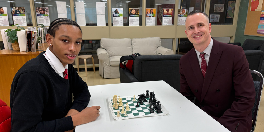 A student and faculty playing chess in a school.