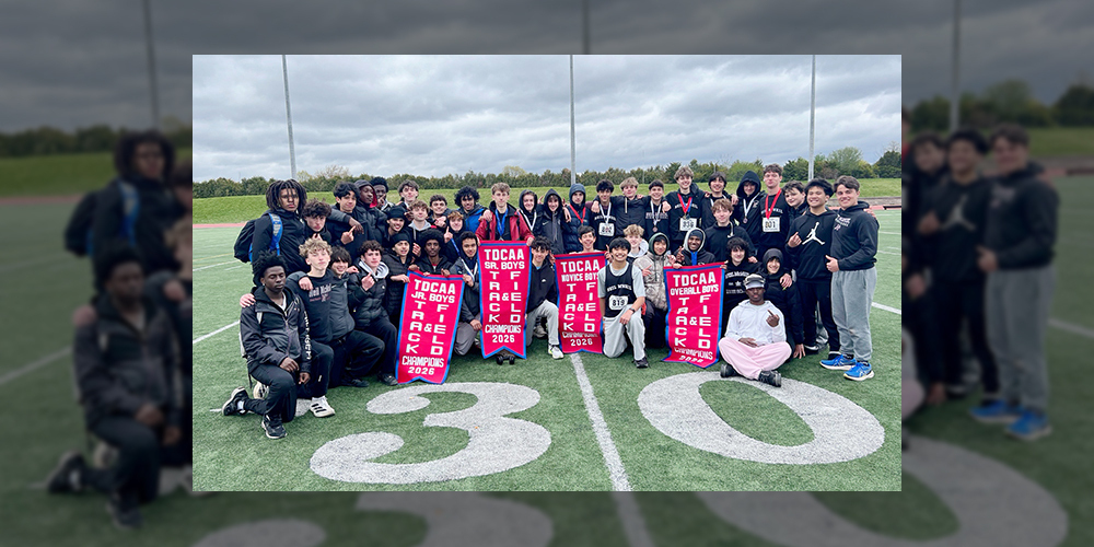 Group photo of the Neil McNeil track and field team on the field with their TDCAA championship banners