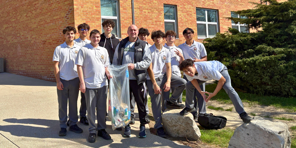 Group photo outdoors of students in uniform with 1 faculty member holding a garbage bag. 