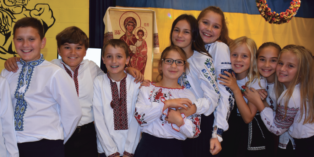 A group of eight elementary school students pose together at a school cultural celebration, wearing traditional embroidered shirts and celebrating Ukrainian Canadian Heritage Month.