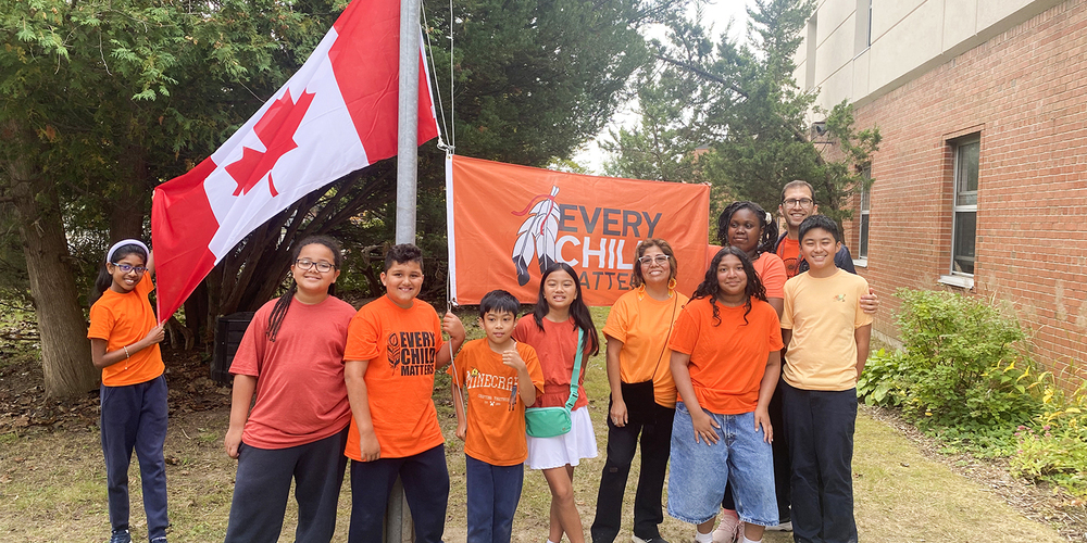 St. Malachy students and staff in orange shirts pose beside a Canadian flag and an “Every Child Matters” banner outside the school in honour of the National Day for Truth and Reconciliation