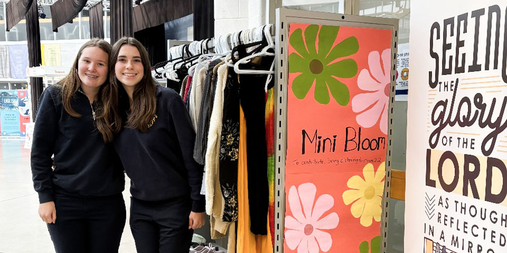 Photo of two Loretto College School students standing next to the Mini Bloom Clothing Rack full of donated clothing items
