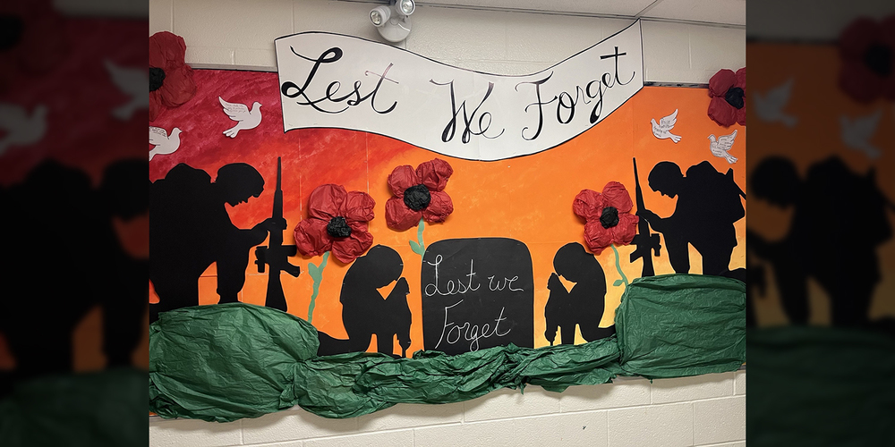 Photo of display for Remembrance Day featuring poppies, silhouettes of soldiers and graves, and the words "Lest We Forget"