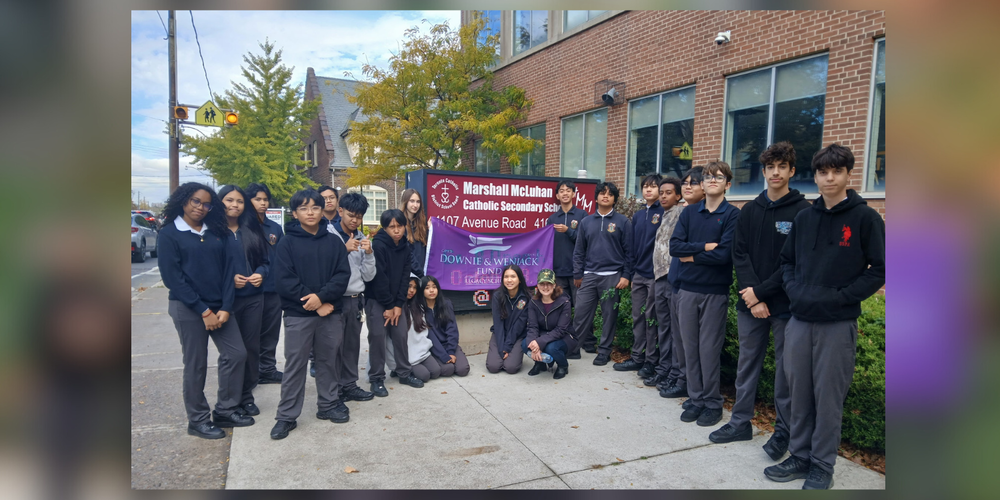 A group of students in uniform posing in front of Marshall McLuhan school