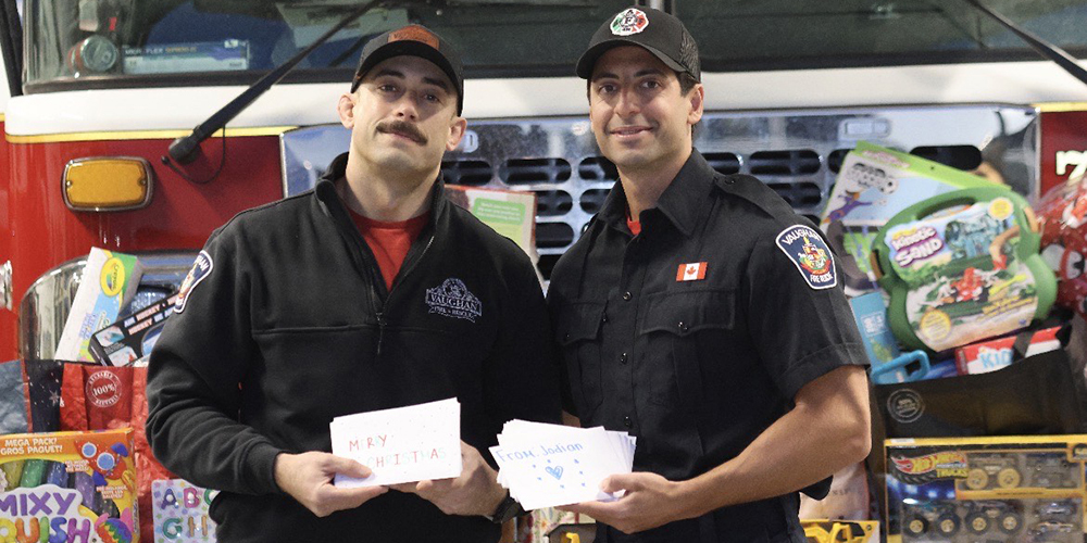 Photo of two firefighters holding up the holiday cards designed by Madonna students