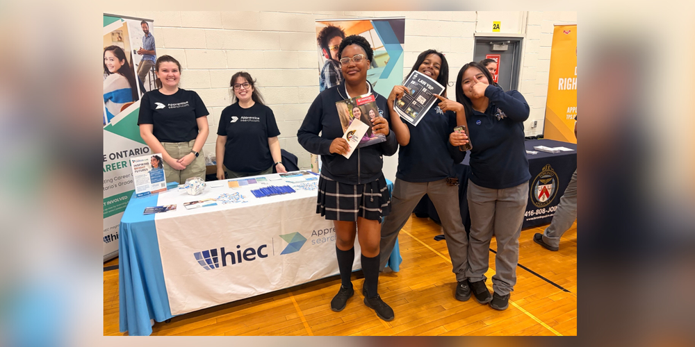 Students posing in front of HIEC display table and representatives