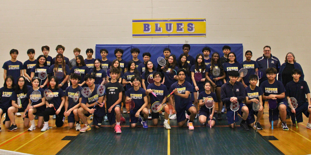 Large group photo of badminton team in a gym.