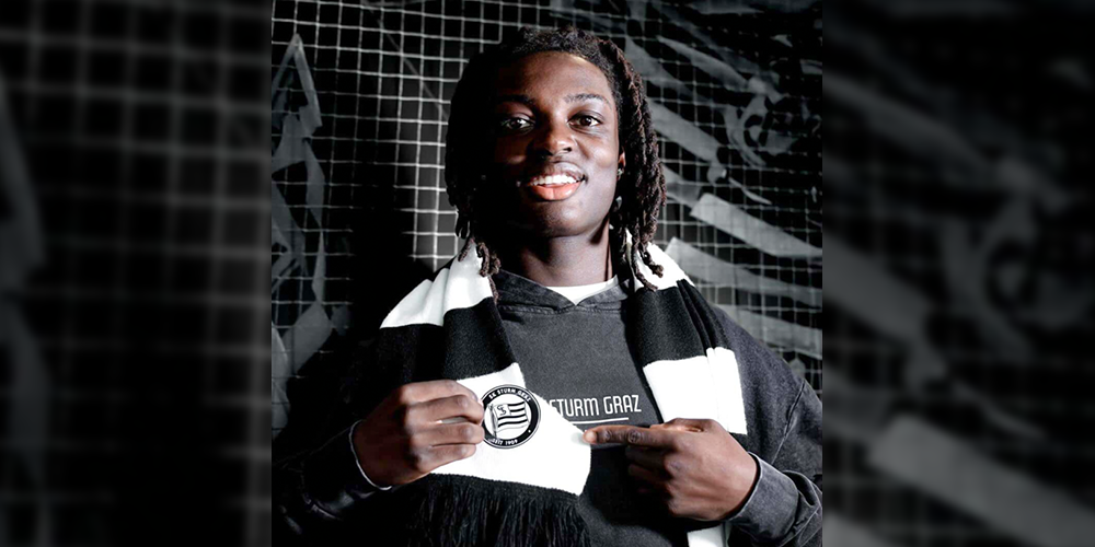 Photo of Elijah wearing a Austrian Soccer Club SK Sturm Graz team scarf and pointing to the club logo on the scarf