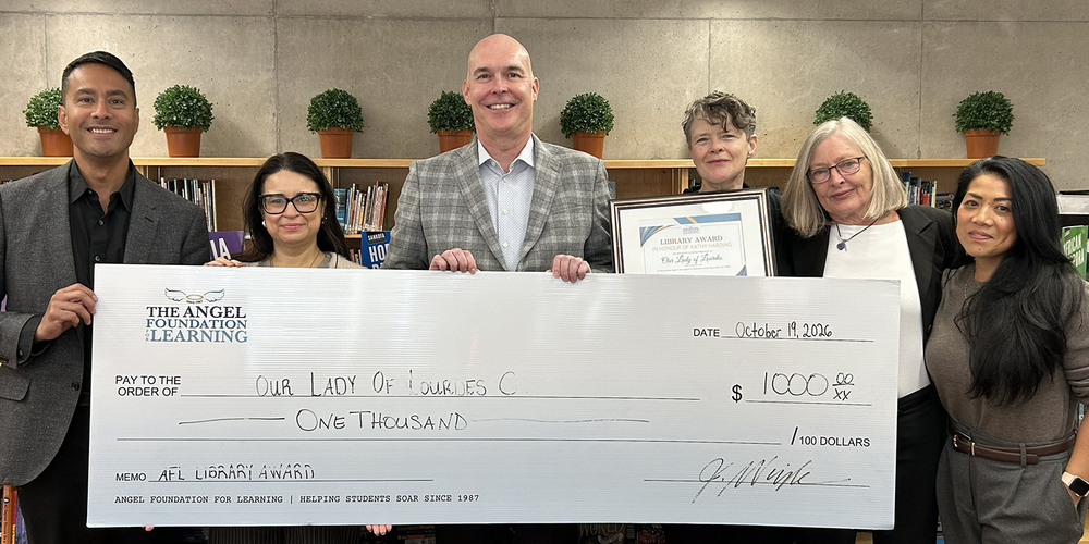 Andrea, in addition Our Lady of Lourdes Catholic School and Angel Foundation for Learning staff pose together with an oversized $1,000 Angel Foundation donation check in an office