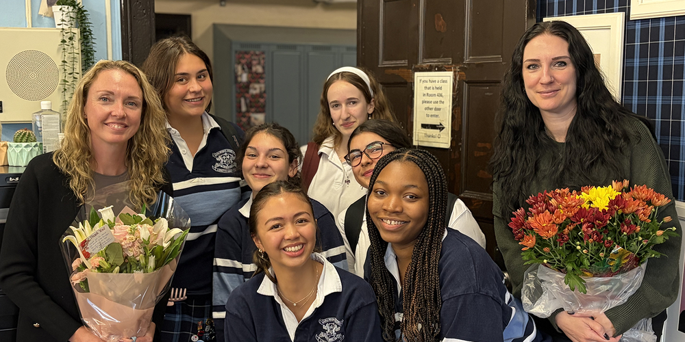 Group photo of Loretto Abbey students in their uniforms, posing with two teachers holding flowers