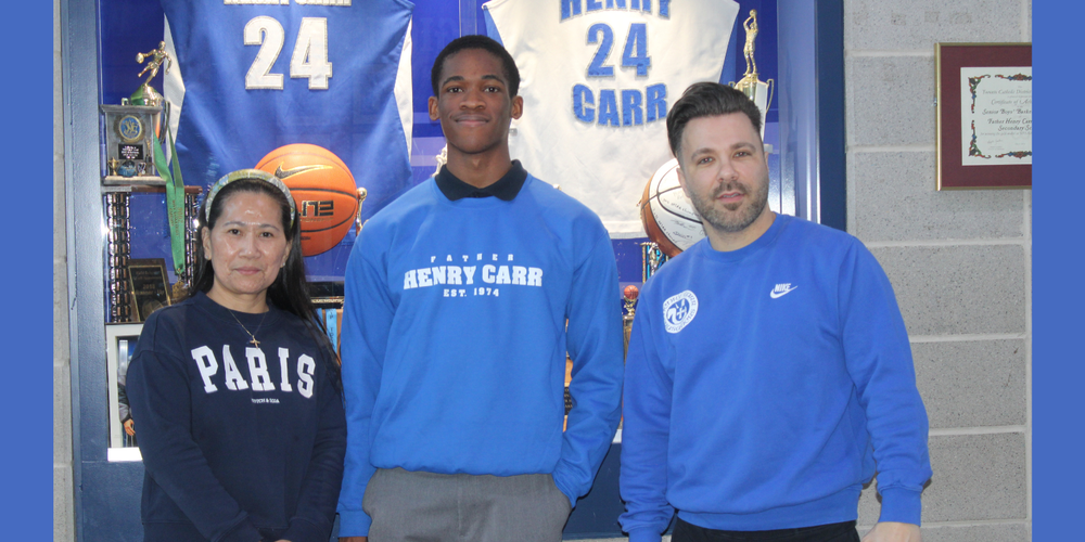 A student and two faculty members posing in front of Father Henry Carr basketball display