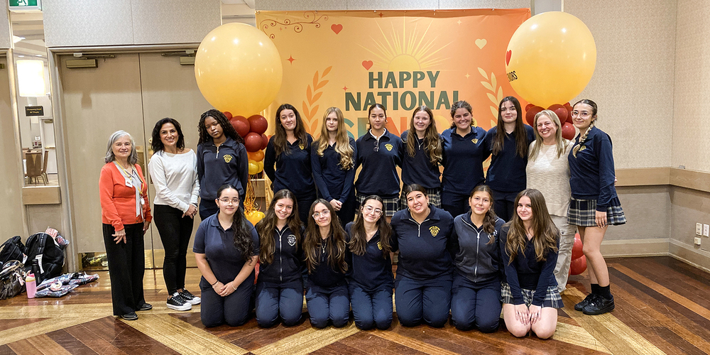 Group photo of Loretto College students posing with staff at Villa Colombo in front of a banner that says Happy National Seniors Day