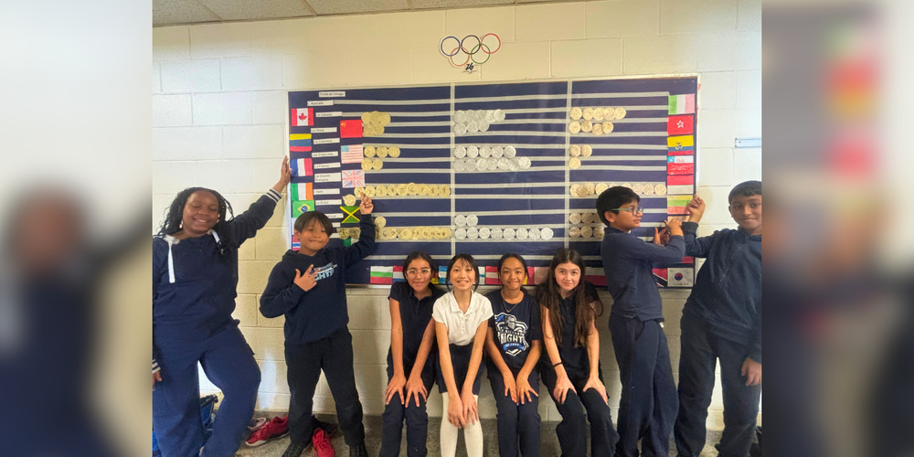 A group of students posing next to a board on the wall with different flags and scores.